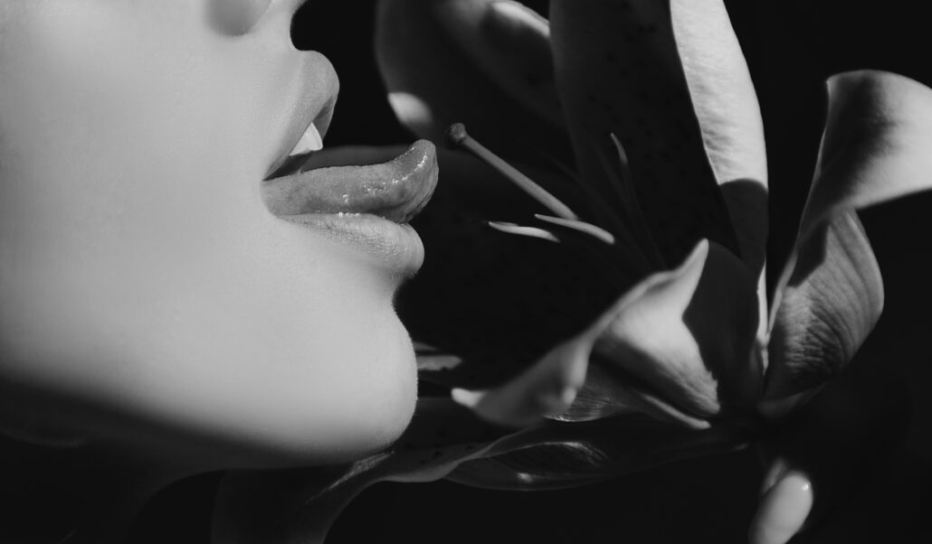 Ein Schwarz-Weiß-Bild, das das Nahprofil einer Person mit leicht geöffneten Lippen in der Nähe einer Lilienblüte zeigt.